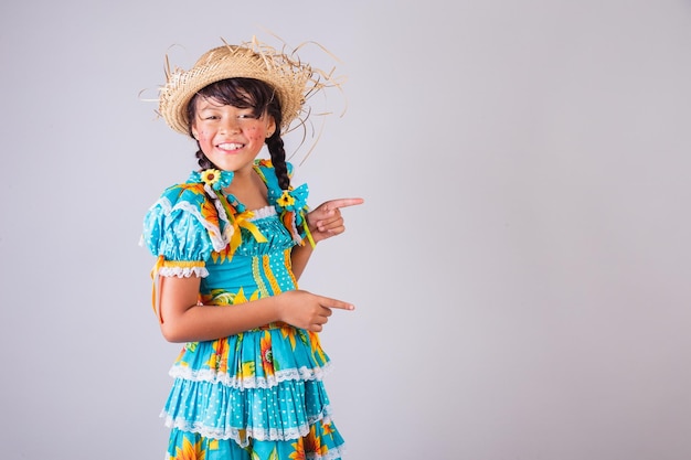 Niña brasileña con ropa de fiesta de junio que muestra algo al lado que presenta un producto de texto o un anuncio