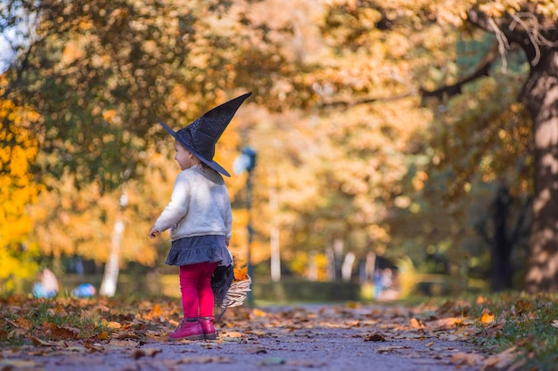 Niña bruja camina en el bosque de otoño con una canasta de hojas