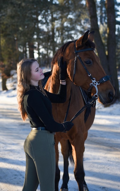 Niña con caballo en el camino del bosque de invierno.