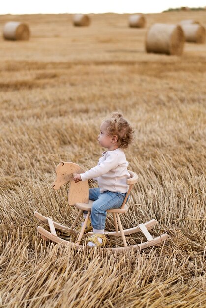 una niña en un caballo de madera. el niño está montando. campo