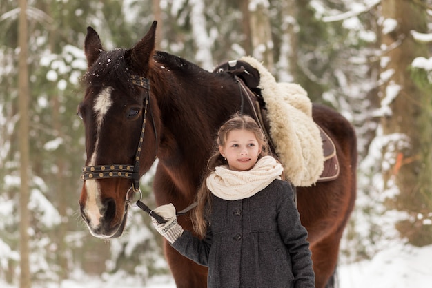 niña y caballo marrón en invierno en la naturaleza