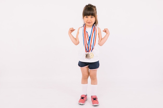 Niña de cabello castaño con medallas de campeones deportivos en el cuello haciendo el símbolo de fuerza. Concepto de deporte y victoria