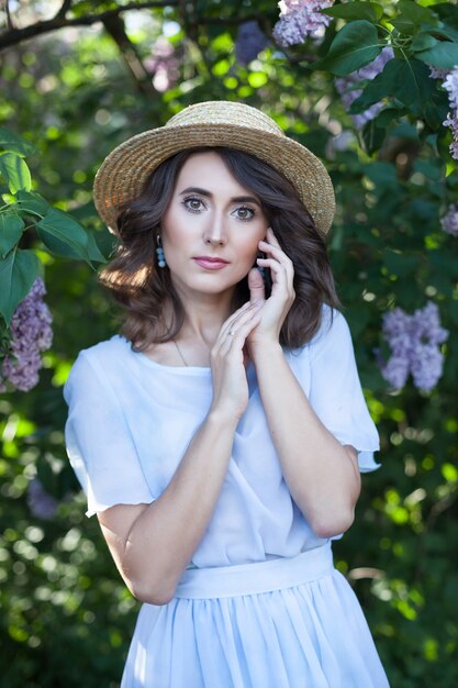 Una niña con cabello castaño ondulado en un sombrero de paja en un jardín lila en flor feminidad vacaciones de verano