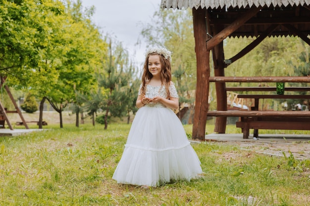 una niña de cabello claro con flores en la cabeza en un vestido blanco sosteniendo anillos de bodas para la ceremonia de boda boda de primavera