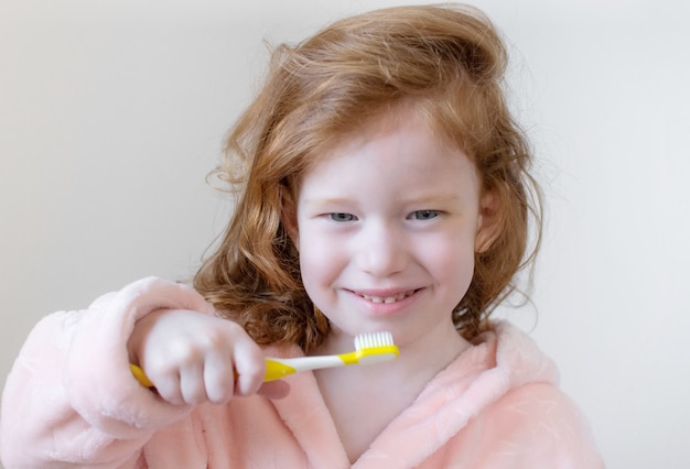 Foto niña con cabello de jengibre cepillarse los dientes, cepillo de dientes amarillo, higiene dental, estilo de vida saludable concepto de estilo de vida nocturno