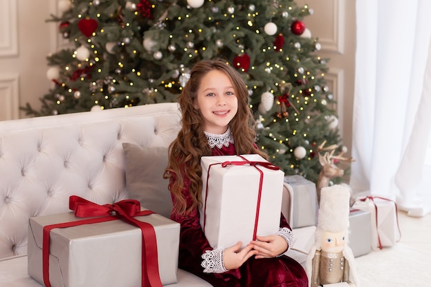 Una niña de cabello largo abre un gran regalo de Navidad en la sala de estar.