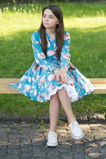 Niña con cabello largo relajándose en el parque día soleado fondo de hierba verde, esperando a alguien concepto.