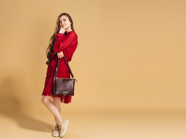 Una niña de cabello largo y rizado con un vestido rojo de verano con una bolsa en sus manos en un color naranja pastel.