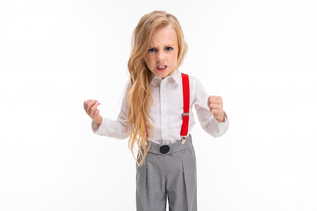 La niña con cabello largo y rubio con una camisa blanca, pantalones rojos, pantalones en una jaula, medias rojas y zapatos con maquillaje brillante está enojada.