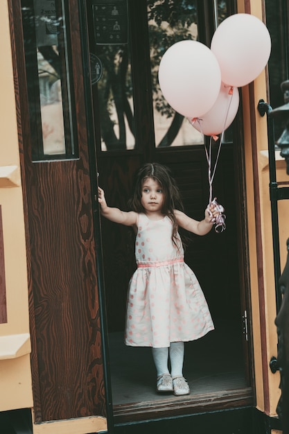 Una niña de cabello largo con un vestido rosa sale del tranvía con globos en las manos. Foto de alta calidad