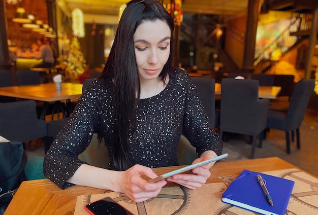 Una niña de cabello oscuro está trabajando en un café con una tableta, un teléfono y un cuaderno cerca. Coworking, organización del flujo de trabajo. Concepto de negocio.