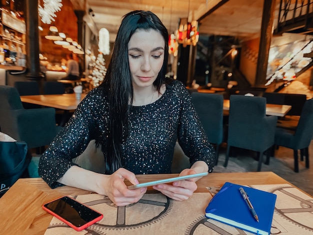 Una niña de cabello oscuro está trabajando en un café con una tableta, un teléfono y un cuaderno cerca. Coworking, organización del flujo de trabajo. Concepto de negocio.