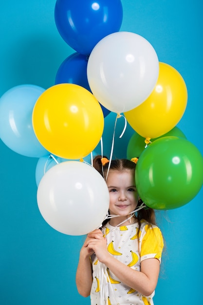 Niña de cabello oscuro con globos de colores sobre fondo azul