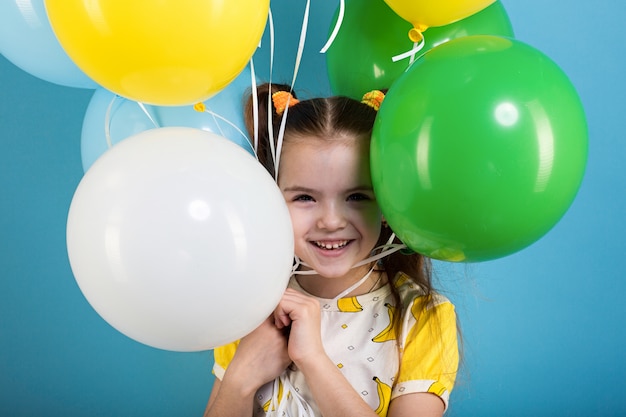 Niña de cabello oscuro con globos de colores sobre fondo azul