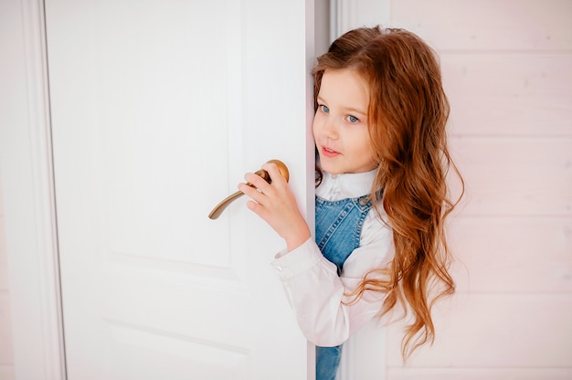 Niña con cabello rizado asoma por la puerta y sonríe