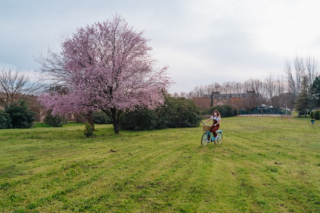 Niña con cabello rizado y una máscara, dando un paseo por un parque con su bicicleta azul