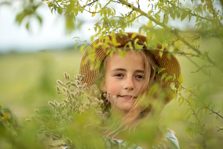 Niña con cabello rizado en un sombrero y flores se encuentra en un vestido largo