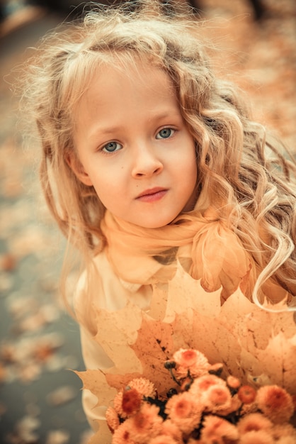 Niña con cabello rubio en otoño de fondo con flores amarillas