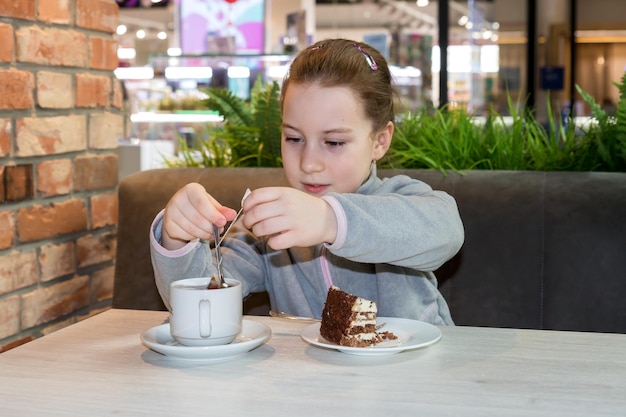 Una niña en un café en una mesa con un postre saca una bolsita de té de una taza