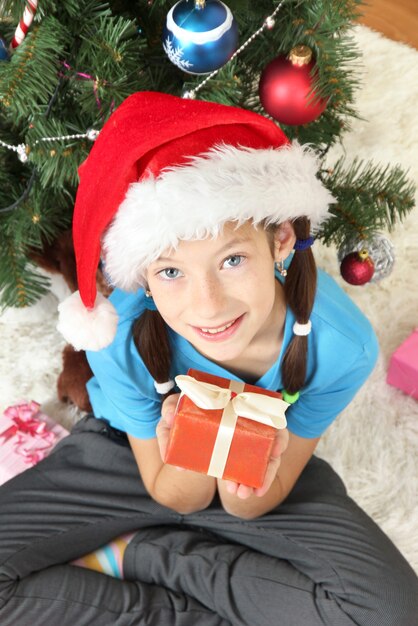 Niña con caja de regalo cerca del árbol de Navidad