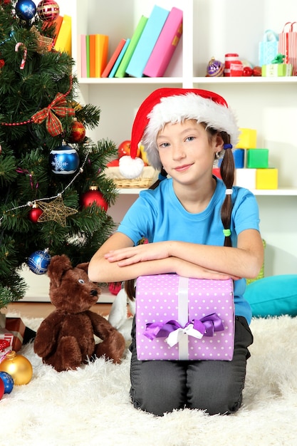 Niña con caja de regalo cerca del árbol de Navidad