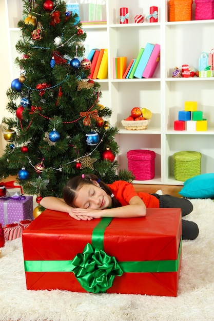 Niña con caja de regalo grande cerca del árbol de navidad