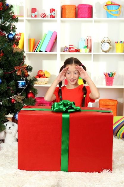 Niña con caja de regalo grande cerca del árbol de navidad