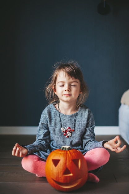 Niña con una calabaza de Halloween en posición de loto