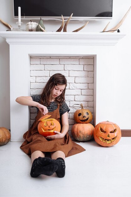 Niña con calabaza tallada en Halloween en casa sentado junto a la chimenea