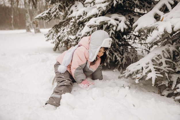 Una niña con un cálido traje de invierno se sienta en la nieve. Niño cerca del árbol de Navidad en invierno. Niño feliz.