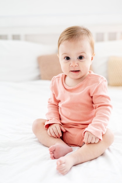 Una niña en una cama en un dormitorio luminoso con un traje rosa sonriendo o riendo