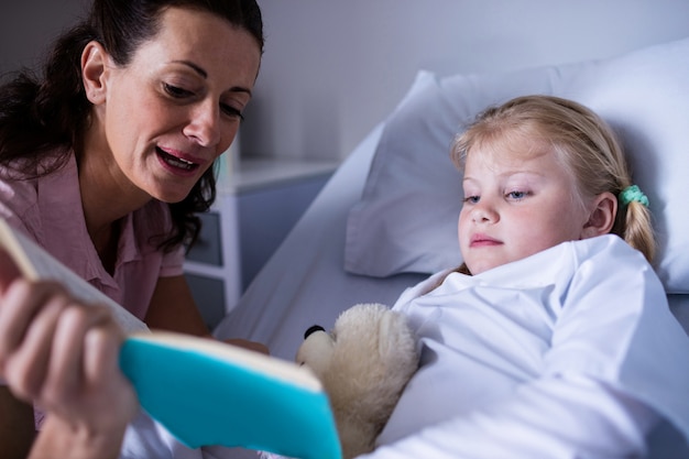 Niña en una cama de hospital leyendo un libro con su madre