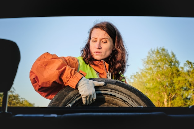 La niña cambia la rueda dañada del coche Chaleco verde Rueda de repuesto Accidente de tráfico