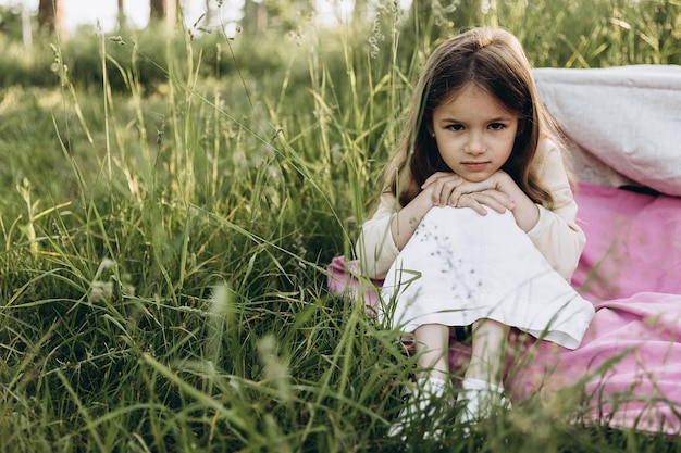 Una niña camina en un bosque de coníferas entre hierba alta antes del atardecer