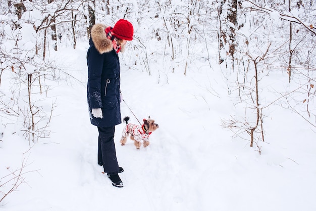 Niña camina en el bosque inferior en invierno con perro vistiendo un suéter de navidad