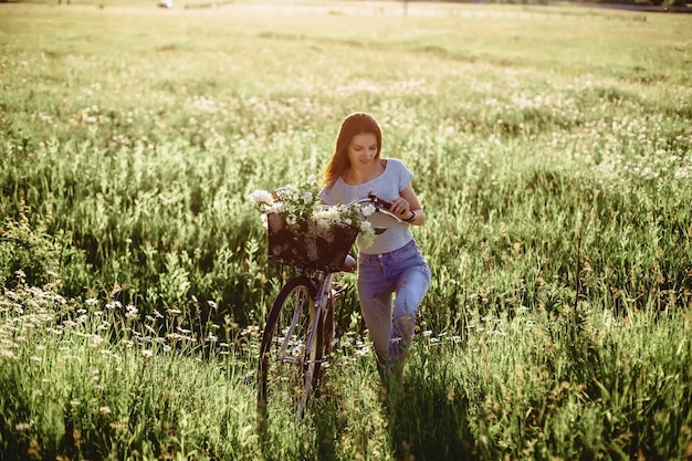 La niña camina con un cachorro en un campo en una bicicleta en la parte trasera de la luz soleada