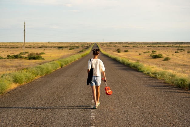 Una niña camina por un camino vacío en la estepa. Tiene un ukelele en las manos.