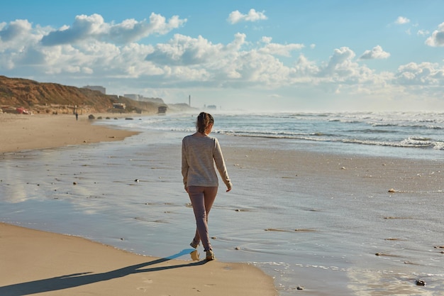 La niña camina por la costa del mar El agua todavía está fría, así que disfruta del paseo