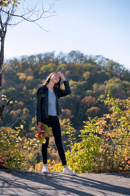 Niña camina en el parque de otoño y disfruta de un día cálido. Retrato de estudiante feliz en el hermoso parque de otoño. Marco vertical.