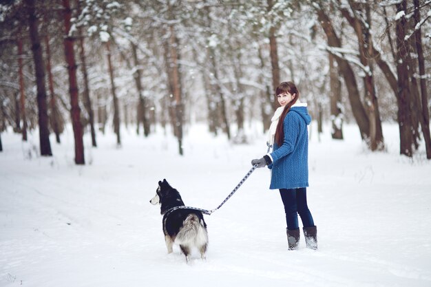 La niña camina con perro husky siberiano en un bosque nevado de invierno