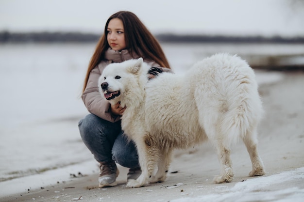 Una niña camina con su querida mascota Samoyed en invierno en la orilla de un lago en el parque caminando el perro en invierno