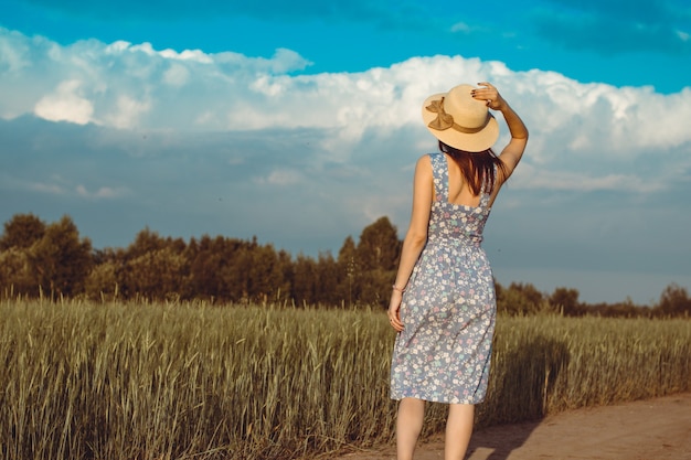 Una niña camina en el verano en un campo donde crece el centeno o el trigo. Ella sostiene un sombrero en sus manos. 6