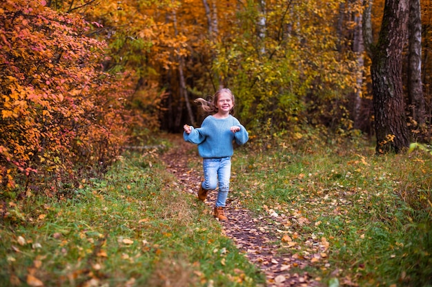 niña caminando en el bosque de otoño con ropa azul