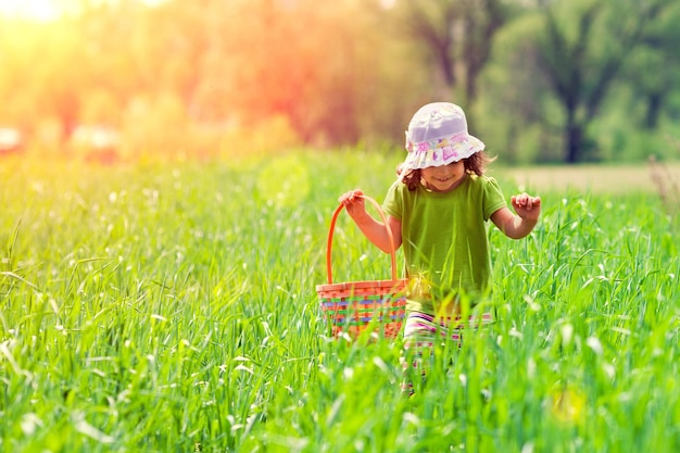 Niña caminando con cesta de picnic en el campo verde