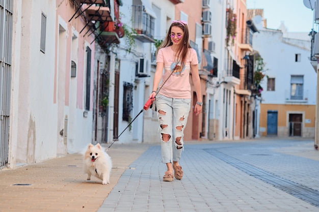 Niña caminando con un pomerania esponjoso blanco.