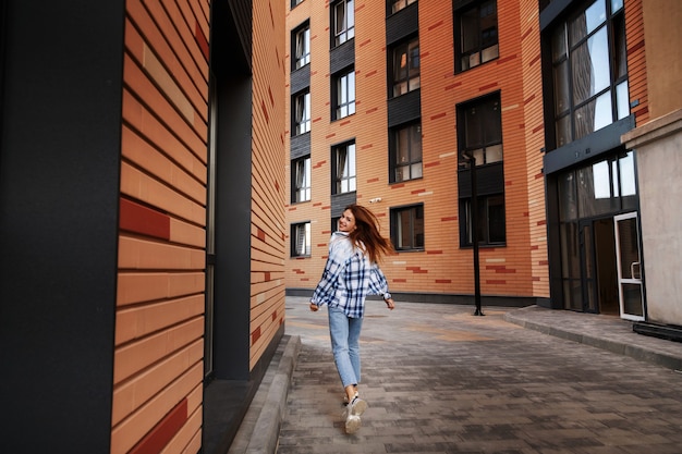 Una niña con una camisa a cuadros corre por la ciudad y sonríe. estilo urbano