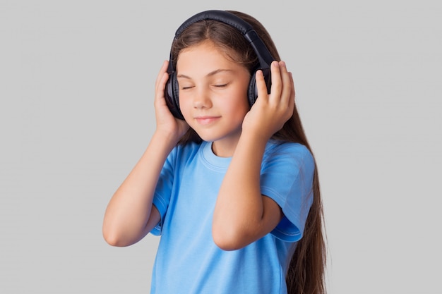 Niña en camiseta azul escuchando música con auriculares inalámbricos y siente placer