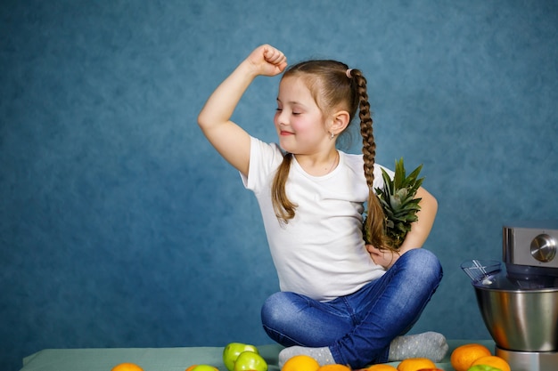 A la niña con una camiseta blanca le encantan las frutas. Ella tiene una piña en sus manos