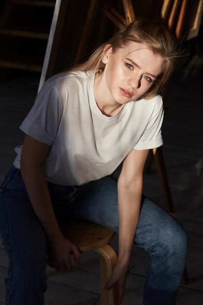 Una niña con una camiseta blanca está sentada en una silla de madera.