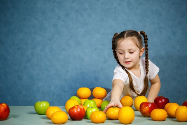 Niña en camiseta blanca juega y posa con fruta